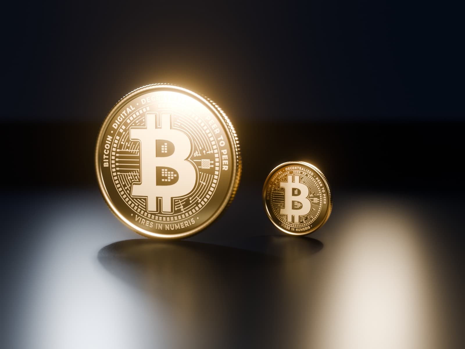 A gold bitcoin coin beside the same coin at half its size